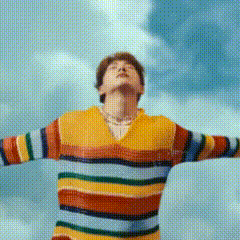a man in a colorful striped sweater is standing with his arms outstretched looking up at the sky .