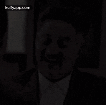 a man in a suit and tie is talking to another man while making a funny face .