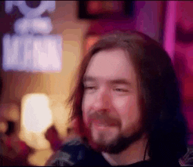a man with long hair and a beard is smiling in front of a sign that says marvel .