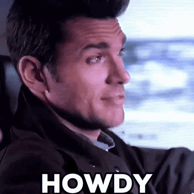 a man is driving a car and making a funny face with the word howdy written on the screen behind him .
