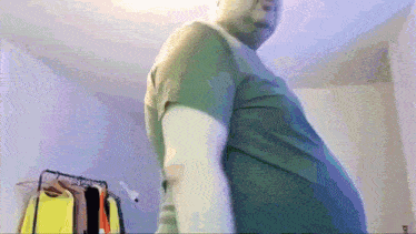a man in a green shirt is standing in a room with clothes hanging on a rack