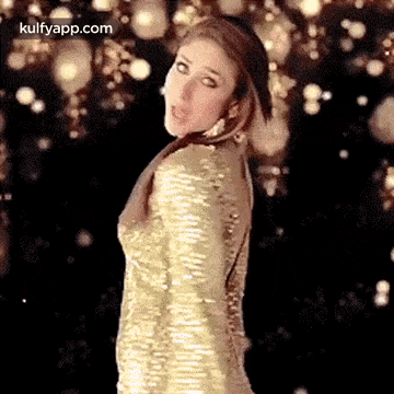 a woman in a gold dress is standing in front of a black background and looking at the camera .