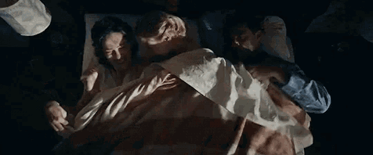 a man and a woman are laying in bed holding hands .