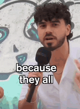a man with a beard is holding a rode microphone and says because they all