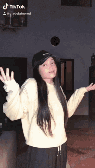 a girl wearing a white sweater and a black hat has a tiktok sticker on her face