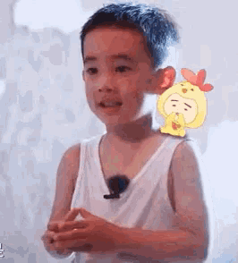 a young boy in a white tank top is standing next to a yellow chicken with a heart on it .