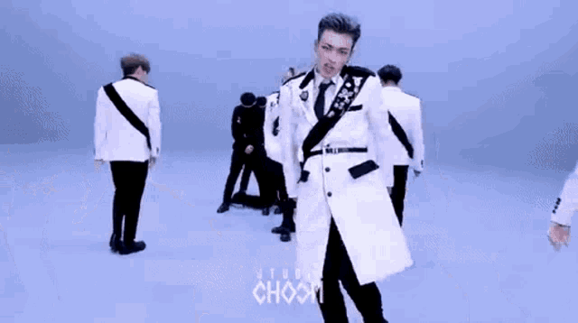 a man in a white suit and tie is dancing with a group of men in black suits .