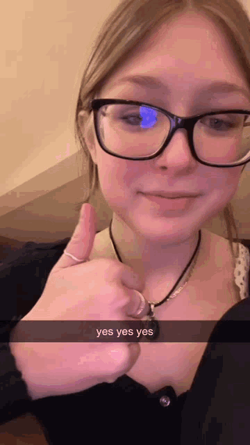 a girl wearing glasses giving a thumbs up with a yes yes yes snapchat