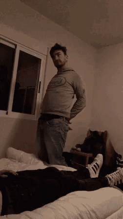 a man is standing in a bedroom next to a window and a bed .