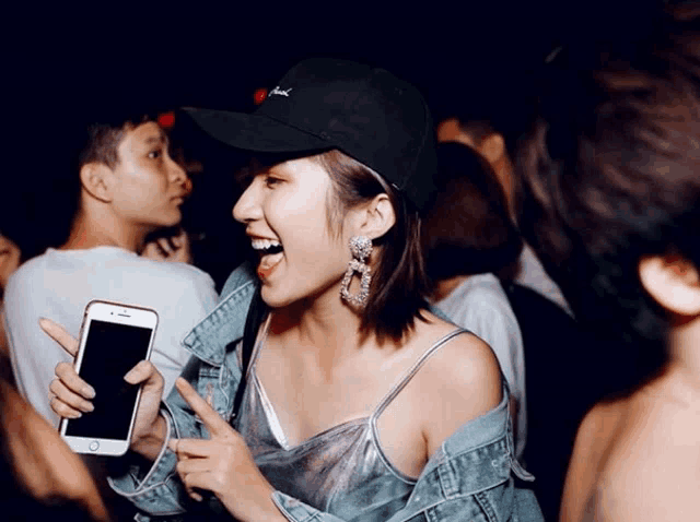 a woman wearing a black hat and earrings is pointing at her phone
