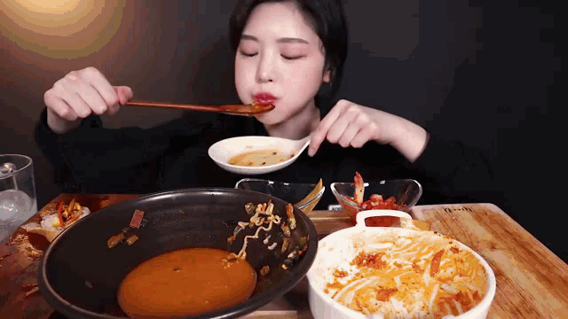 a woman is sitting at a table eating food with a spoon .