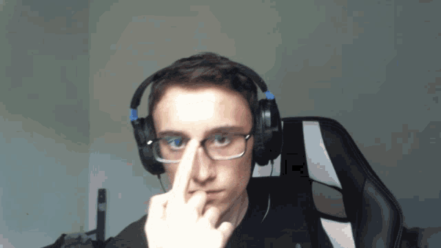a young man wearing headphones and glasses is pointing at his nose
