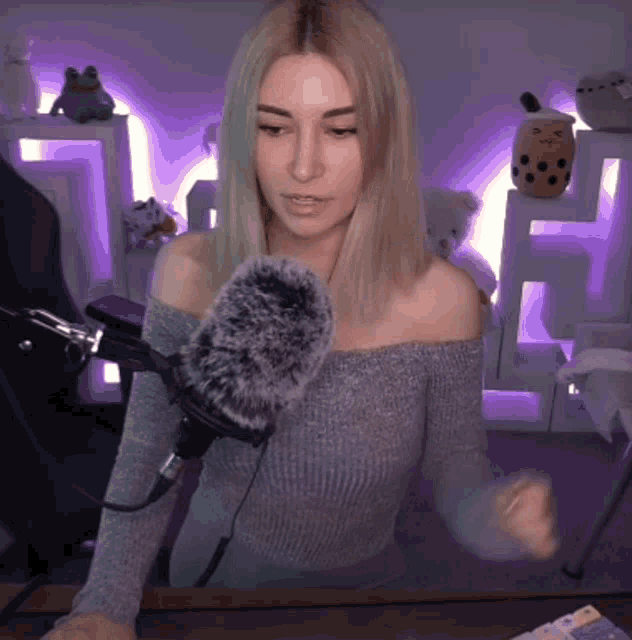 a woman wearing a grey off the shoulder sweater is sitting in front of a microphone .