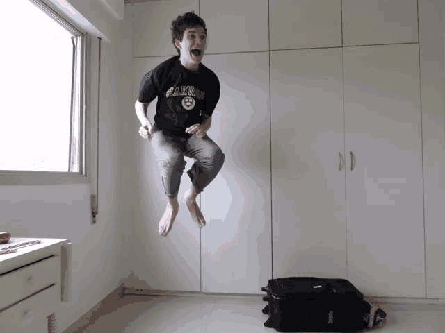 a young man wearing a harvard shirt jumps in the air