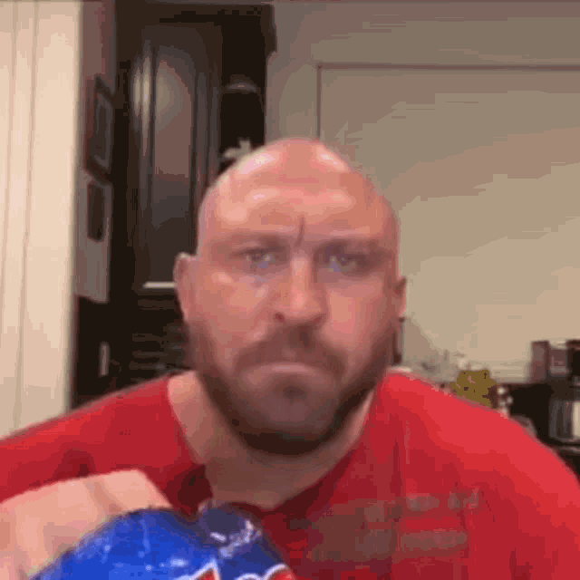 a bald man with a beard is holding a bag of chips and looking at the camera .