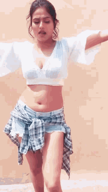 a woman in a white crop top and plaid shorts is standing in front of a wall