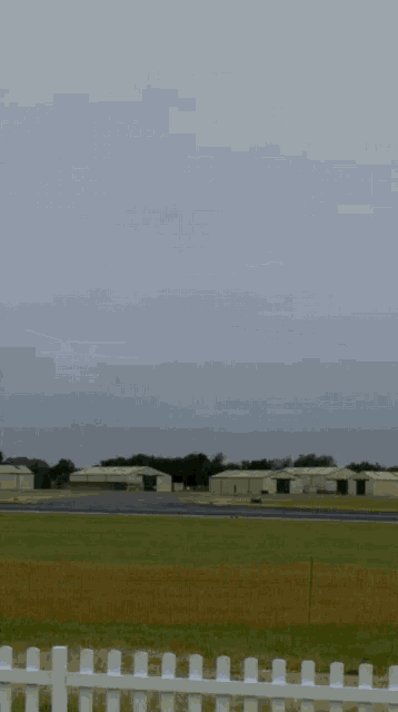 a field with a runway and buildings in the background