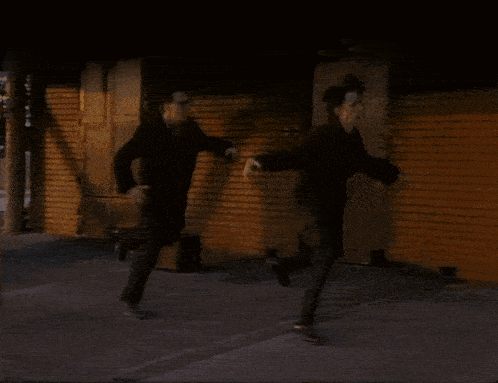 a man in a black suit is walking down a sidewalk