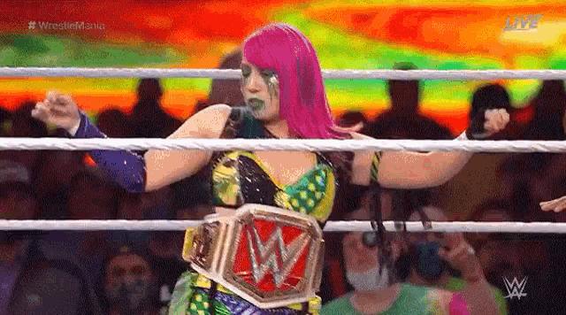 a woman with pink hair is standing in a wrestling ring holding a wrestling belt .