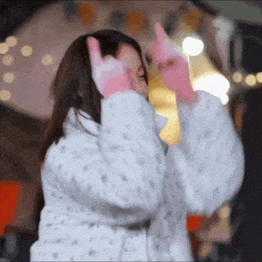 a woman wearing a white coat and pink gloves is making a peace sign with her hands