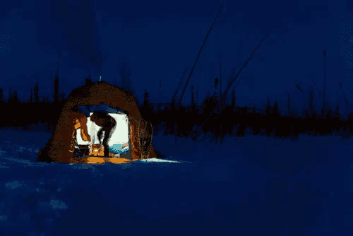 a tent is lit up in the middle of a snowy field at night