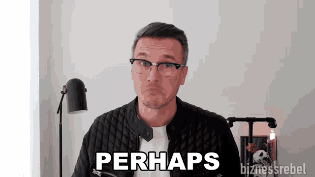 a man wearing glasses and a leather jacket says perhaps in front of a white wall