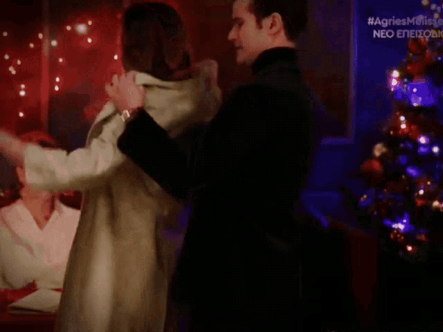 a man and woman dancing in front of a christmas tree