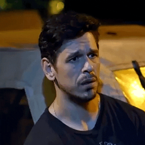 a man with a beard is making a funny face while sitting in front of a car at night .