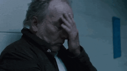 a man is sitting in a dark room with his hands on his head .