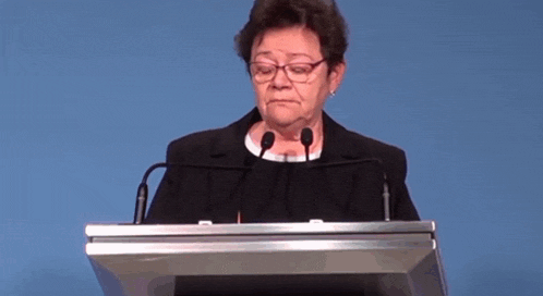 an older woman is standing at a podium with two microphones