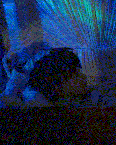 a blurry picture of a person laying on a bed with a blue and green light behind them
