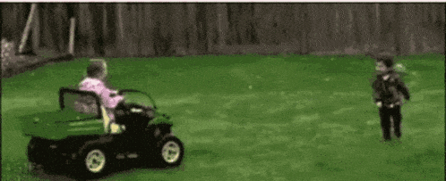 a little girl is riding a green lawn mower on a lush green lawn .