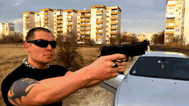 a man with a tattoo on his arm is holding a gun in front of a car