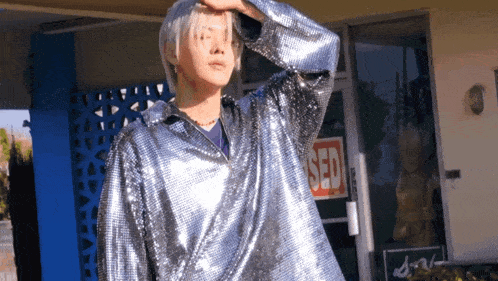 a man in a silver sequined jacket stands in front of a building with a red sign that says sed