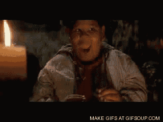 a man is sitting in front of a lit candle and making a funny face .