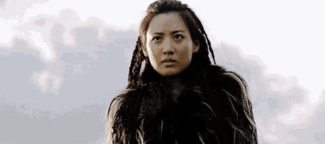 a woman with dreadlocks wearing a fur coat looks up at the sky
