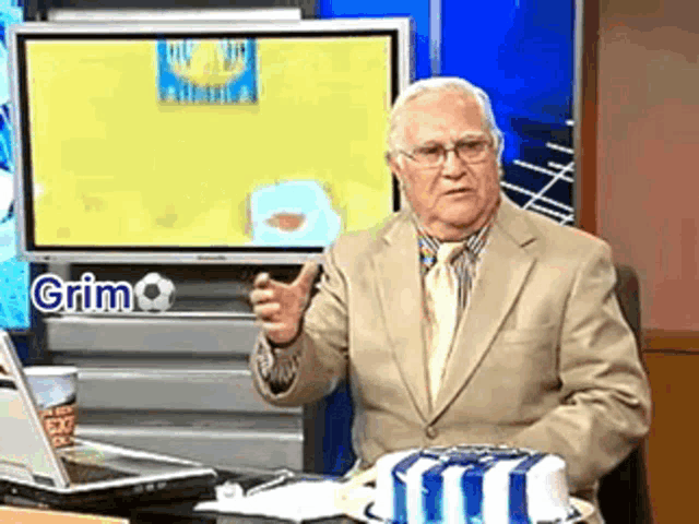 a man in a suit and tie is sitting in front of a tv screen that says grim