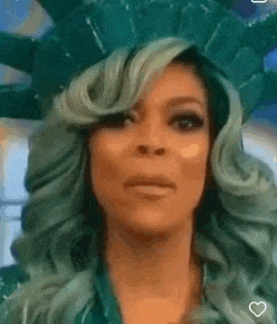 a woman with green hair is wearing a statue of liberty costume and making a funny face .