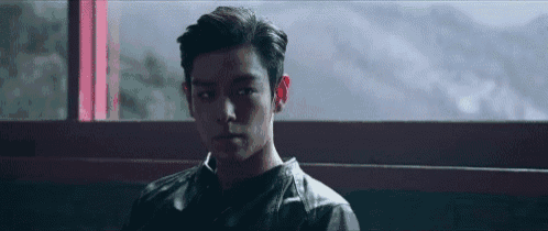a young man in a leather jacket is looking out a window .