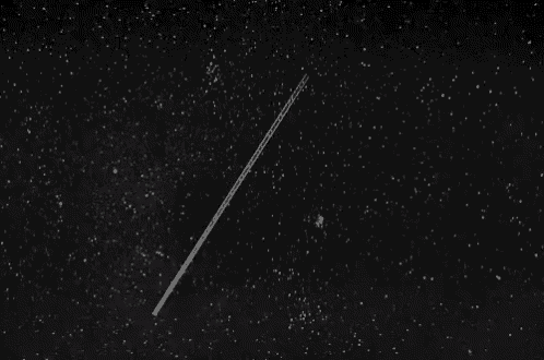 a black and white photo of a starry night sky with a shooting star .