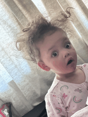 a baby with a surprised look on her face is wearing a pink unicorn pajama top