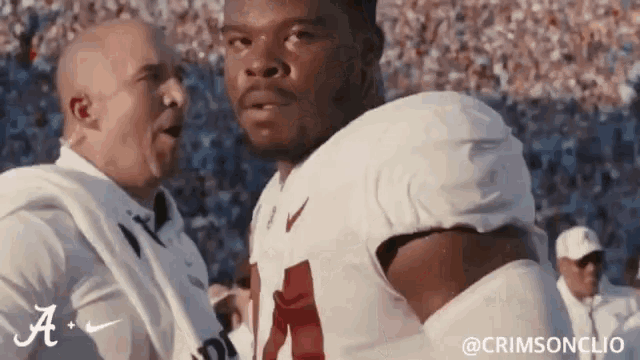 a man in a white shirt is talking to a football player in a white uniform .