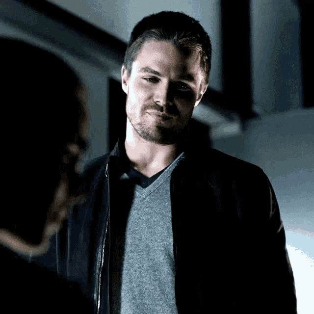 a man with a beard wearing a grey sweater and a black jacket