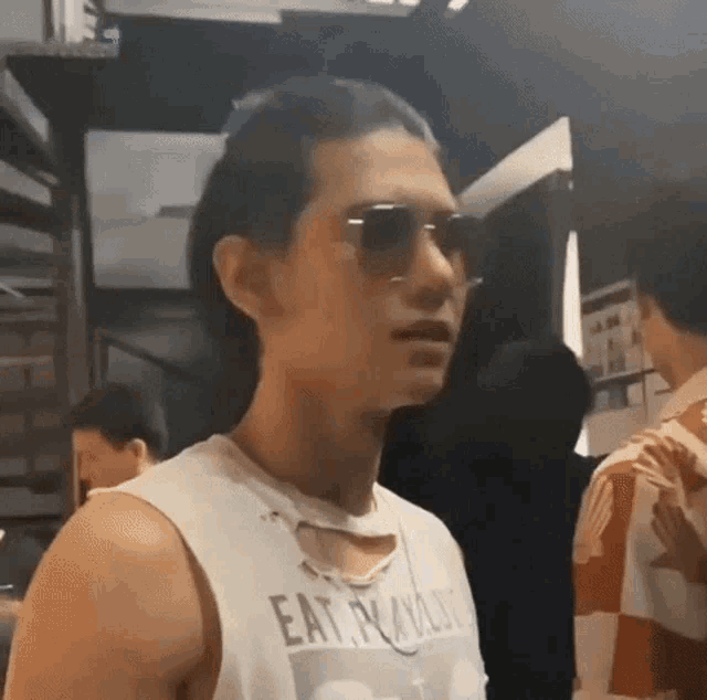 a man wearing sunglasses and a white tank top that says eat noodles