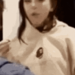 a close up of a woman wearing a white hoodie eating a sandwich .