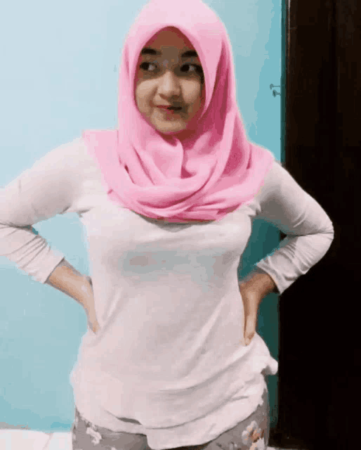 a woman wearing a pink hijab and a white shirt has her hands on her hips