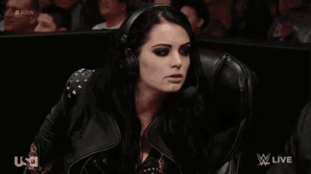 a woman wearing headphones and a leather jacket is sitting in a chair in front of a crowd .