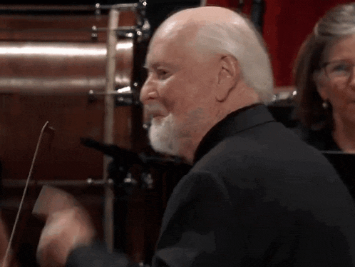 a man with a beard is playing a violin in front of an orchestra