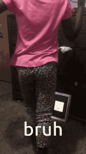 a woman in a pink shirt and leopard print pants is standing in front of a sign that says bruh on it