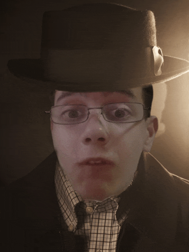 a man wearing glasses and a fedora looks at the camera with a surprised look on his face